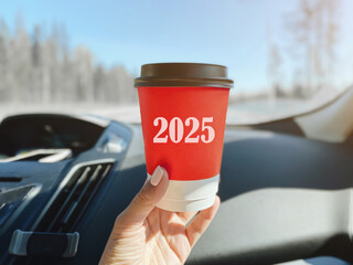 red paper cup with the inscription text 2025 with a hot drink in the hand of a girl who is sitting...