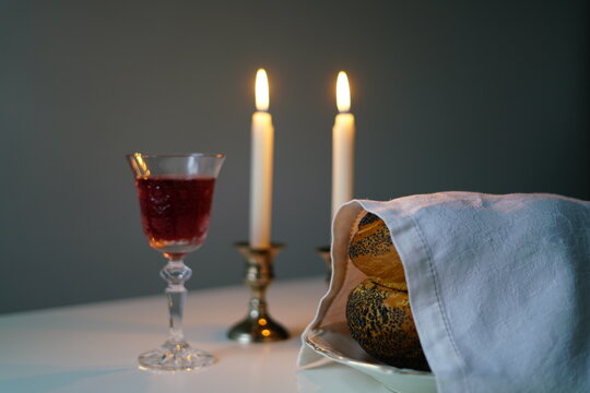 Shabbat or Sabbath kiddush ceremony composition with a traditional sweet fresh loaf of challah bread, glass of red kosher wine and candles on a vintage wood table with copy space