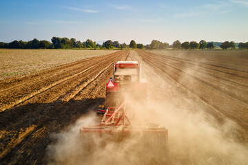 Fototapeta premium Red tractor working in agricultural field, cultivating and plowing dry soil, aerial view. Agribusiness concept. Small farming concept