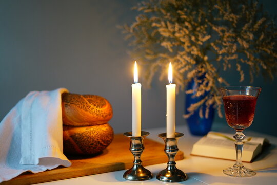 Shabbat or Sabbath kiddush ceremony composition with a traditional sweet fresh loaf of challah bread, glass of red kosher wine and candles on a vintage wood table with copy space