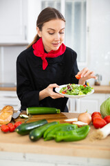 Satisfied female chef in black uniform demonstrating excellent salad in kitchen