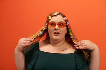 Dressed in a stylish outfit, a plus size woman playfully styles her colorful hair accessories.