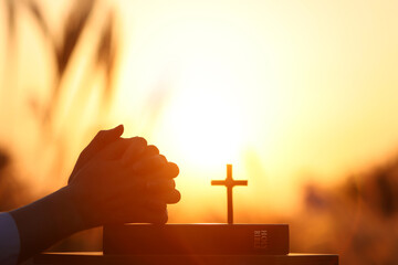 Christian praying with both hands together on the holy bible, autumn barley field sunset landscape, thanksgiving easter background
