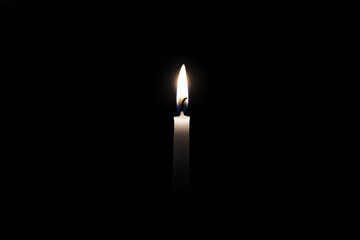Single candle is lit in a dark room. The candle is the only source of light in the room