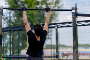 Naklejka premium on the street in park near the horizontal bars a nice guy brunette in black shorts and a black T-shirt does pull-ups on the horizontal bar healthy lifestyle muscle pumping