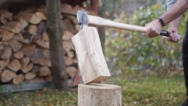 Chopping birch wood on a log block, axe in action. Slow-motion captures chips flying. Firewood neatly stacked in the yard on a sunny day.