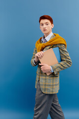 A young man with striking red hair displays an elegant winter outfit while confidently holding a notebook.