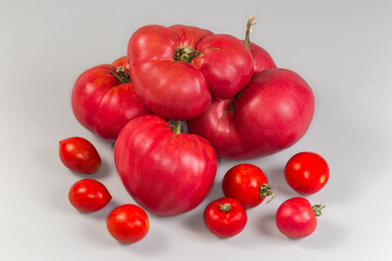 Big ribbed pink tomatoes and cherry tomatoes on gray background