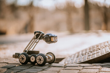 A small inspection robot with wheels and a camera is positioned near an open manhole, ready for...
