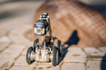 A close-up of a wheeled inspection robot with a camera, positioned on pavement near an open manhole, used for sewer and infrastructure inspections..