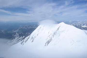 A stunning rock formation covered in snow, set against a clear blue sky with fluffy clouds in the background, creating a peaceful and breathtaking mountain landscape.