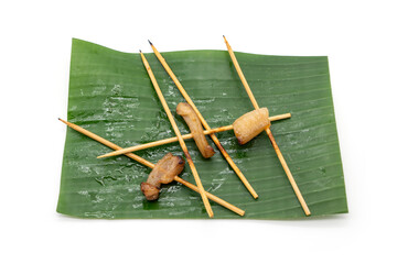 Leftover skewers on the banana leaf of Grilled pork sticks and pork fat stuck to them from people who don't like to eat it isolated on white background.