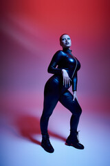 A young woman with short pink hair and a nose piercing strikes a fierce pose against a colorful backdrop.