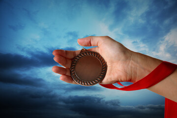 Woman holding bronze medal in hand against sky, closeup