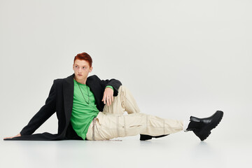 A young, handsome man with striking red hair showcases bold fashion choices in a studio environment.