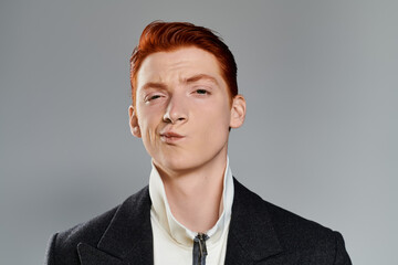 A confident young man with red hair showcases his winter style, exuding charm in a neutral setting.