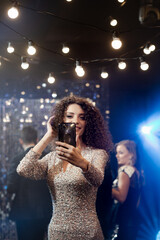 young beautiful woman takes a selfie at a party. she is wearing an evening dress. In the background are her colleagues and friends. party concept