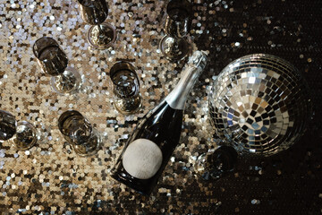 a champagne glass against a background of a blurred composition of glasses and bottles, which creates an atmosphere of anticipation of the holiday. A glittery disco ball in the center enhances the fee