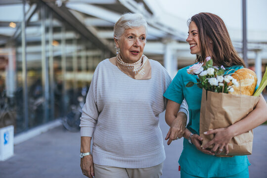 Caring Nurse Assisting Elderly Woman With Groceries Outdoors