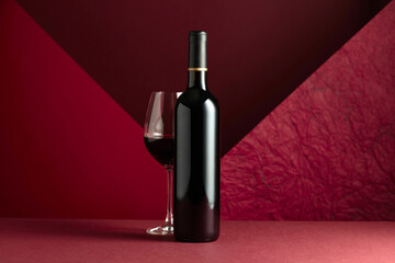 Bottle and glass of red wine on a red background.