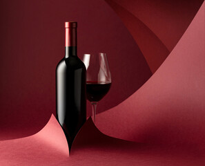 Bottle and glass of red wine on a red background.