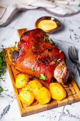 Baked pork knuckle with potatoes and cheese sauce on the cutting board vertical photo