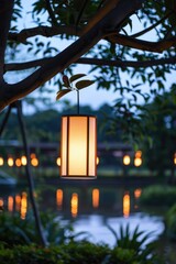 A lantern hangs from a tree branch above a serene lake at sunset