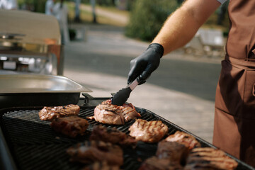 Chef grilling steaks outdoors at a sunny barbecue event in a park, showcasing culinary skills