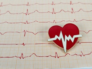 A red heart pin resting on an electrocardiogram chart showing heartbeat patterns