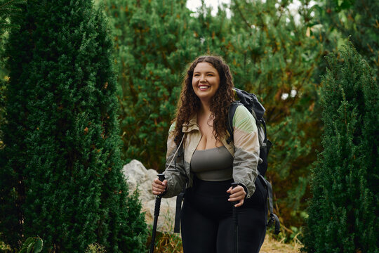 A cheerful plus size woman walks through a lush forest, embracing natures beauty and adventure.