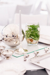 Elegant table setting with silver accents and a decorative glass filled with green ferns and white flowers