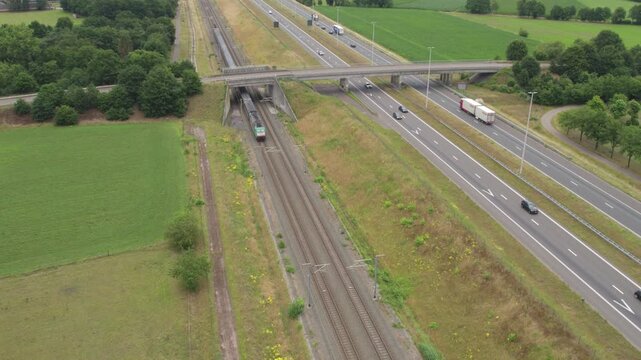 E19, Brecht, Antwerpen, Belgium, 15th of June, 2024, An aerial view showcases a train smoothly running close to a highway that is surrounded by lush green fields and trees