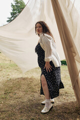 The beautiful plus size woman stands confidently in a field, draped in flowing fabric.