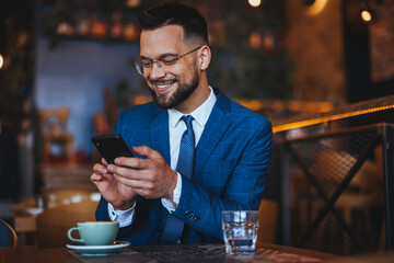 Businessman Smiling While Checking Phone in a Modern Cafe