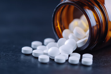 White pills scatter dramatically across a dark surface, spilling from an overturned bottle in disarray