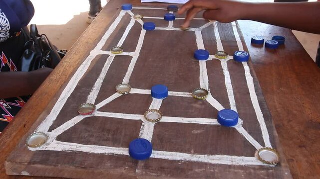 Traditonal african strategy board game know as morabaraba or muravarava being played on a wooden board using recycled bottle cap pieces