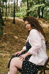 A stunning plus size woman relaxes on a chair amidst the lush beauty of nature in the woods.