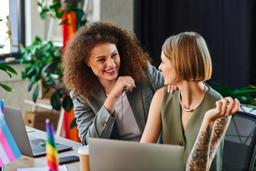 Two coworkers enjoy a light moment, embracing their identities in a welcoming workspace.