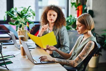 Two coworkers share ideas at a colorful office workspace, celebrating diversity and teamwork.