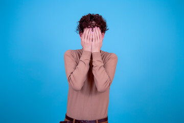 A funny young attractive guy with a curly hairstyle poses in the studio.