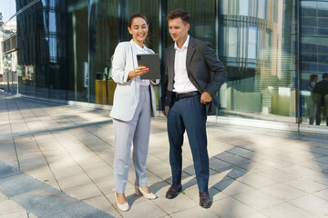 Business Professionals Review Data on a Tablet Outside a Modern Office Building in Bright Daylight