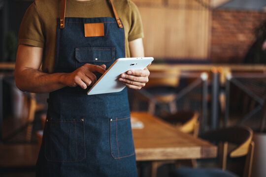 Barista in Apron Using Tablet in Coffee Shop Setting