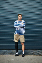 A young man with crossed arms showcases his prosthetic leg against a modern backdrop.