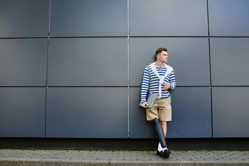 A young handsome man leans against a sleek wall, showcasing his stylish attire and prosthetic leg.