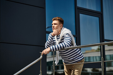 A young man with a prosthetic leg leans pensively on a balcony railing, embracing the sun.