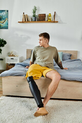 A young man with a prosthetic leg sits thoughtfully on a bed, surrounded by warm decor.
