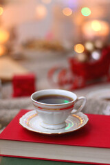 Various Christmas decorations, lit candles, cup of tea or coffee, cookies, books, presents and soft blanket on the table. Holiday hygge at home. Selective focus.