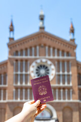 Hand holding an Italian passport with a traditional Italian urban landscape in the background