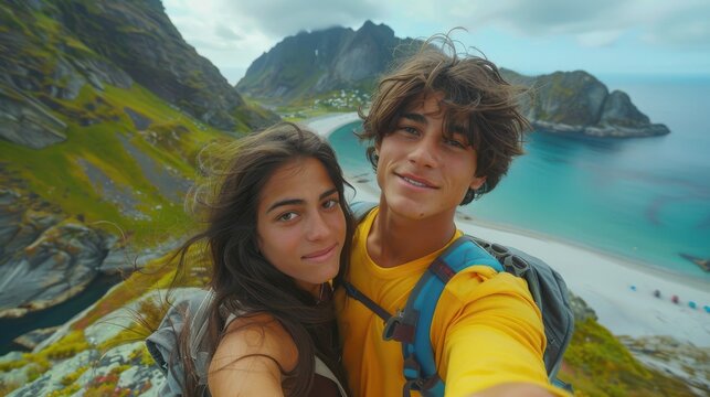 A young couple takes a joyful selfie with a scenic background of mountains and a tranquil seaside, capturing an adventurous moment in nature.