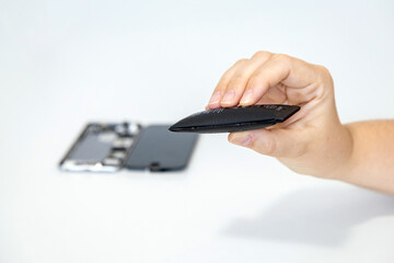 Hand holding a swollen phone battery with a disassembled phone blurred in the background